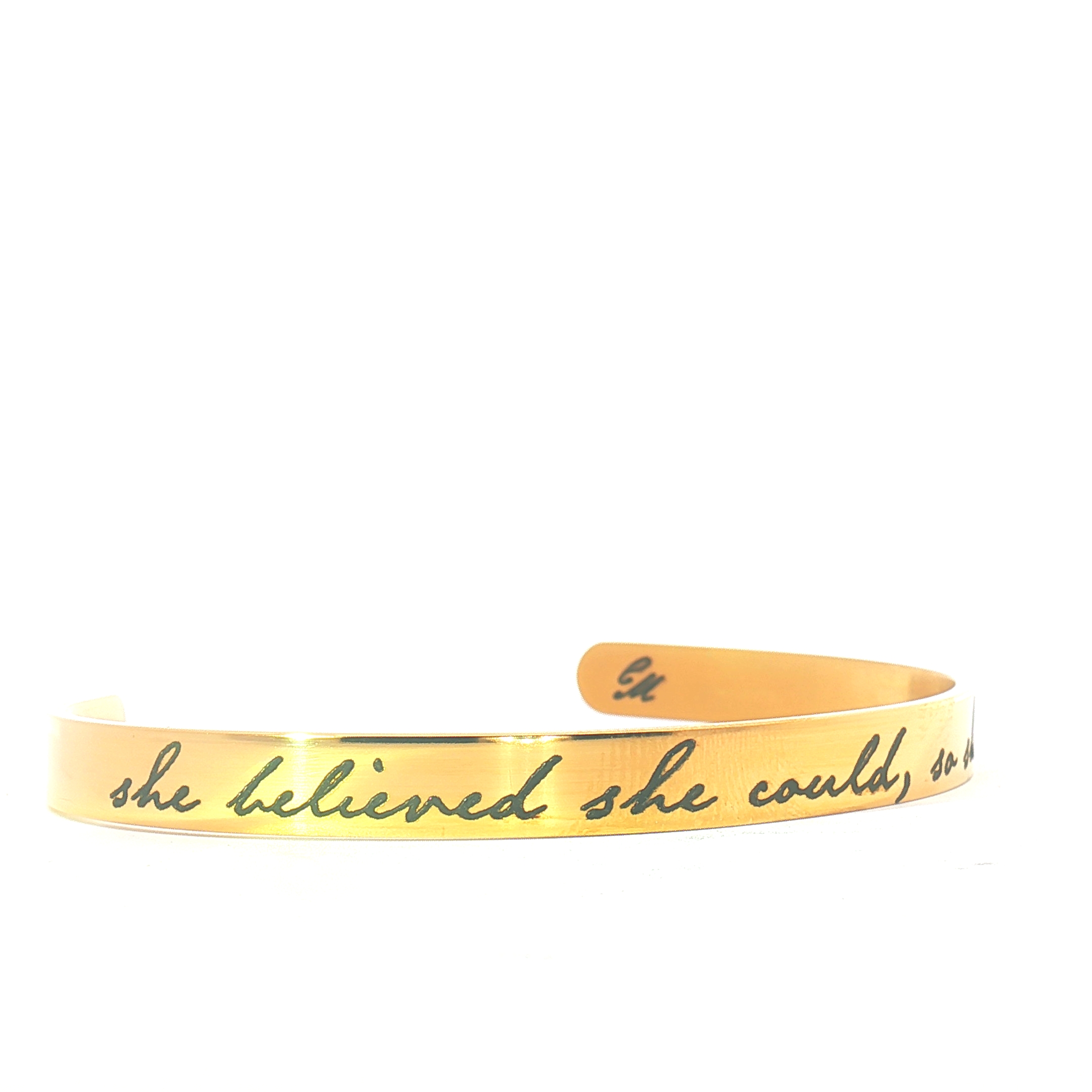 A gold bracelet with engraved cursive text that reads, she believed she could, so she did, set against a plain white background.